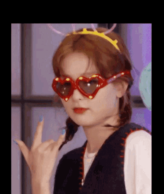 a woman wearing heart shaped sunglasses and a yellow headband is making a rock sign .
