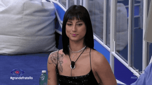 a woman is sitting in front of a window with a bottle of water in front of her and the words grandefratello on the bottom
