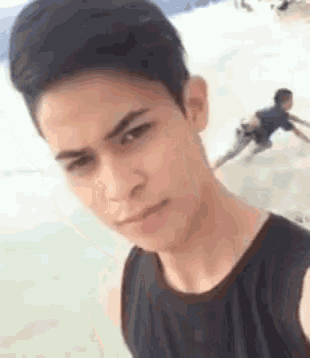 a young man in a black tank top is taking a selfie at the beach .