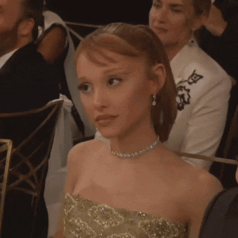 a woman in a strapless gold dress is sitting in a chair at a dinner table .