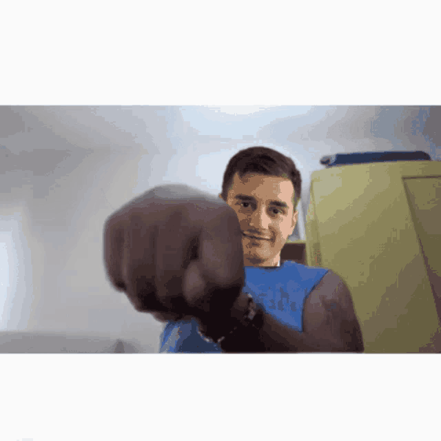 a man wearing a blue tank top is giving a fist bump