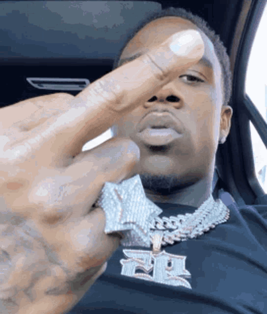 a man wearing a necklace and a ring is giving the middle finger