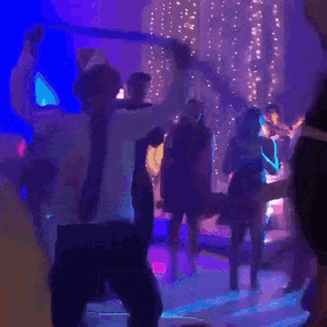 a group of people dancing in a dark room with purple lights