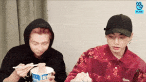 two young men are eating noodles with chopsticks from a bowl that says supreme