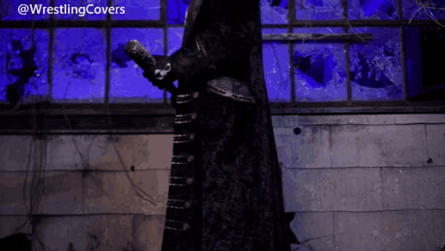 a man in a black coat is standing in front of a window with a blue light behind him and the words wrestlingcovers above him