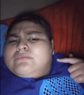a young boy in a blue shirt is pointing at his chest