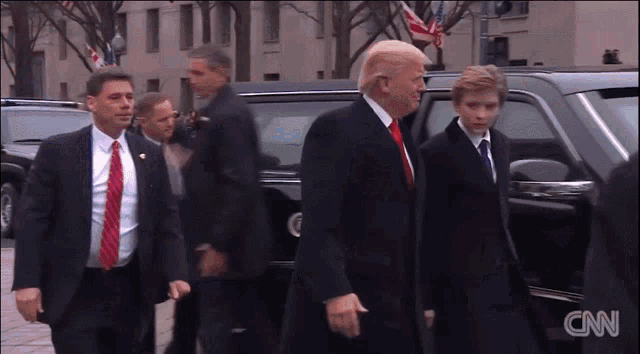 a man in a suit and tie is walking towards a cnn car