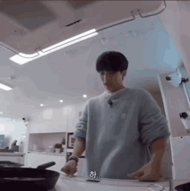 a man in a light blue sweater is standing in a kitchen cooking .