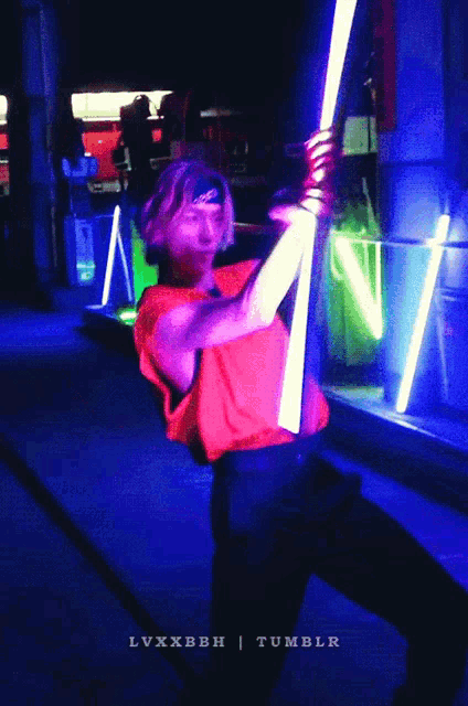 a man in a red shirt is holding two lightsabers in front of a blue background that says tumblr