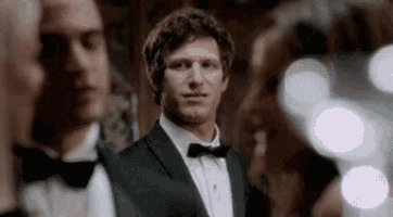 a man in a tuxedo and bow tie is standing in a room with other people .