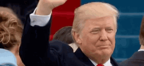 donald trump is raising his hand in the air while sitting in a crowd of people .