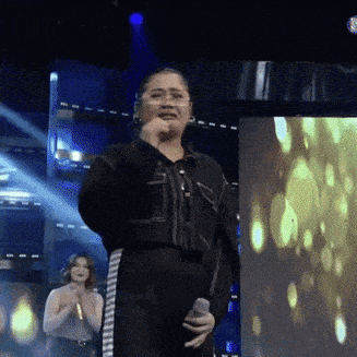 a woman singing into a microphone on a stage in front of a screen