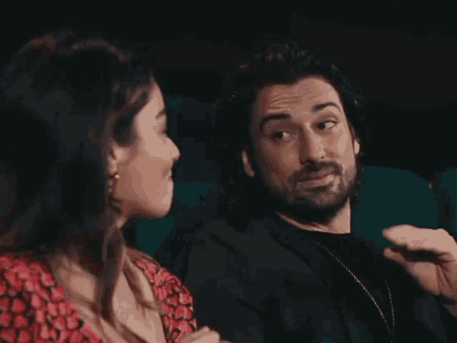 a man and a woman are sitting next to each other in a movie theater and talking to each other .