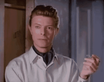a man in a white shirt and tie is smoking a cigarette while standing in front of a door .