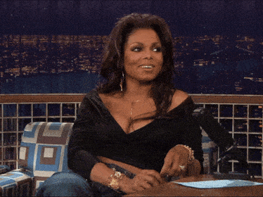 a woman laughs while sitting in front of a late night show