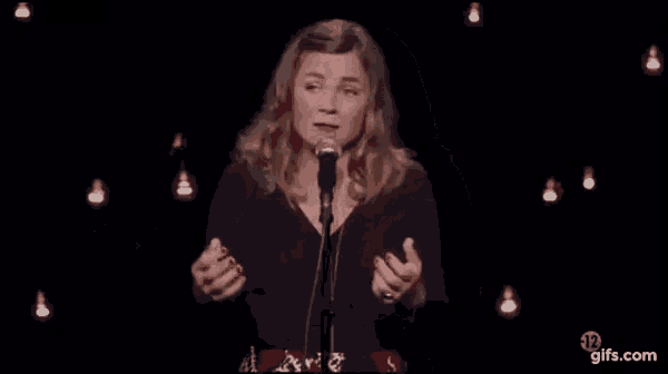a woman is singing into a microphone on a stage in front of a crowd .