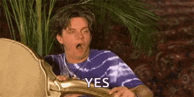 a man in a purple tie dye shirt is holding a chair with his mouth open and says yes .