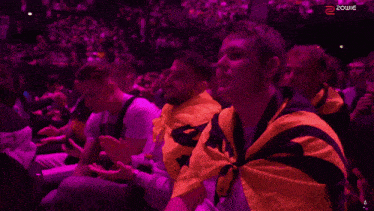 a group of people sitting in a stadium with a purple light behind them that says zowie