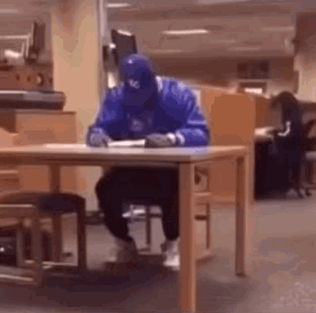 a man in a blue jacket is sitting at a desk in a library .