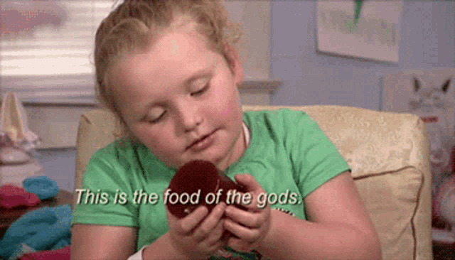 a little girl in a green shirt is holding a red apple and says this is the food of the gods