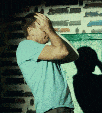 a man in a blue shirt holds his head in front of a wall with train pictures