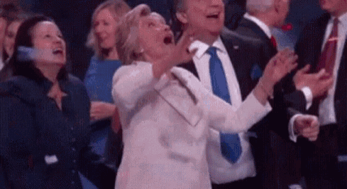 a woman is screaming in a crowd of people while a man in a suit and tie is clapping .
