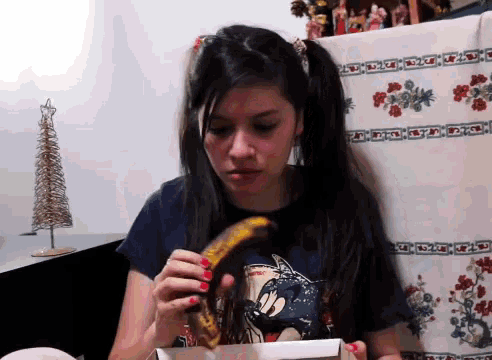 a girl wearing a mickey mouse shirt holds a banana