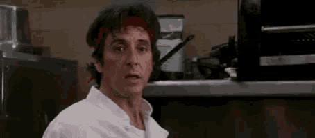 a man in a chef 's uniform is standing in a kitchen with a red headband .