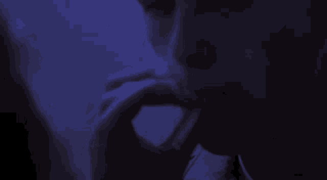 a woman is smoking a cigarette in a dark room with a blue light behind her .