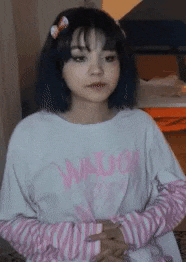 a girl with blue hair and a pink shirt is standing with her hands on her hips .