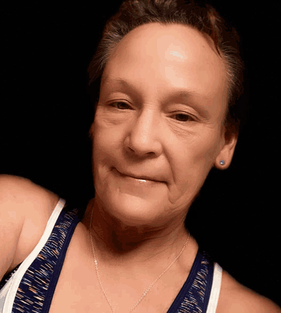 a woman wearing a blue and white tank top and a necklace smiles for the camera