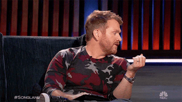 a man with a beard is sitting on a couch in front of a screen that says songland