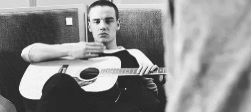 a man is sitting in a chair holding an acoustic guitar .