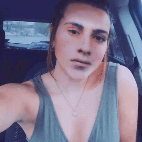 a woman in a green tank top is taking a selfie in the back seat of a car