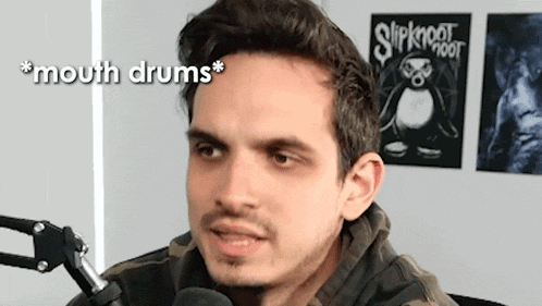 a man is talking into a microphone in front of a wall with slipknot posters on it .