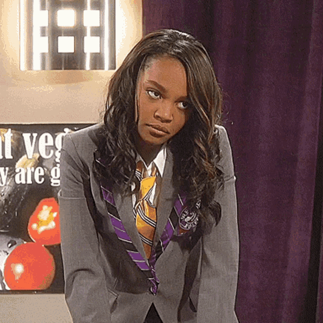a woman in a suit and tie stands in front of a sign that says " vegetables are good "