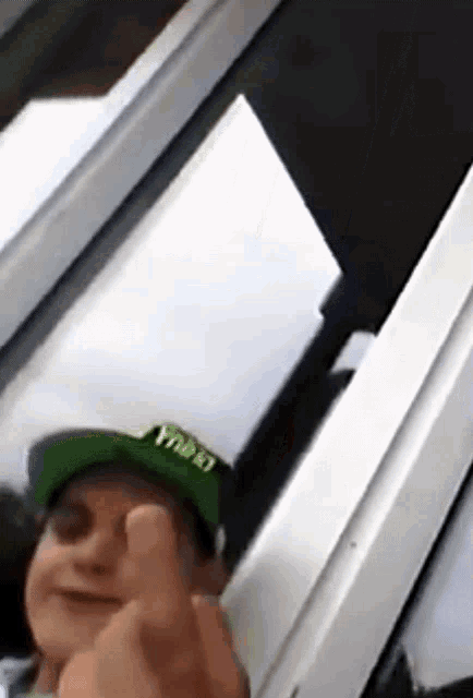 a man wearing a green hat with the word yacht on it is giving the middle finger .