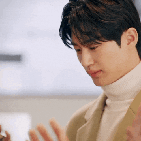 a man wearing a white turtleneck and a tan jacket looks down