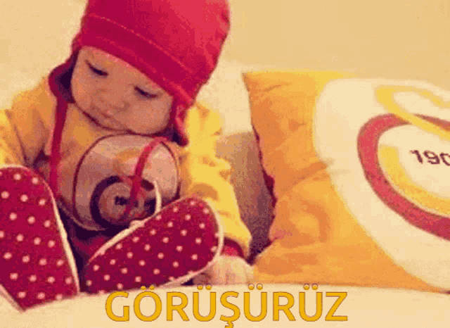 a baby wearing a red hat and polka dot socks sits on a bed next to a pillow that says 190