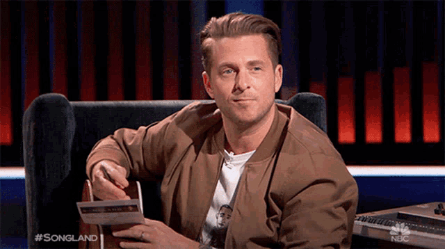 a man is sitting in a chair holding a piece of paper that says songland