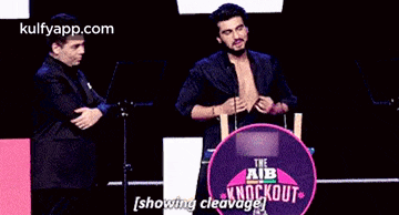 two men are standing next to each other on a stage and one of them is showing his chest .