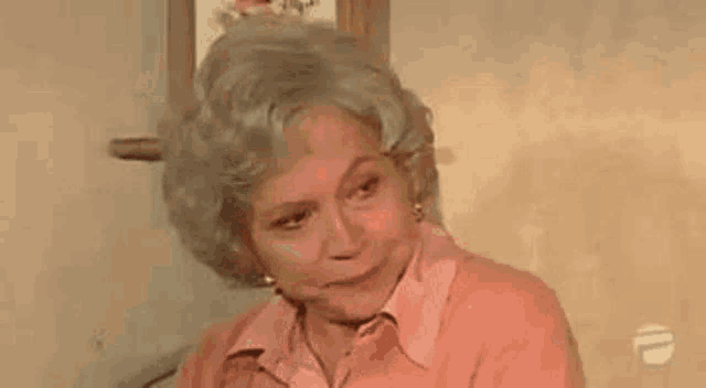 an elderly woman is sitting in a chair in front of a wall with a picture of flowers on it .