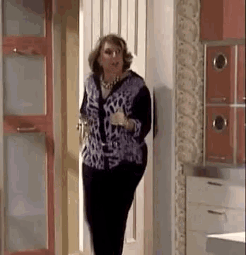 a woman in a purple shirt and black pants is standing in a doorway .