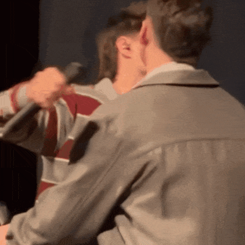 a man in a striped shirt is holding a microphone while another man looks on