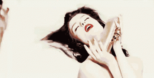 a woman with her eyes closed is holding a bottle of perfume in her hand .