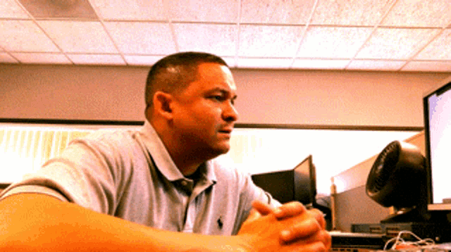 a man wearing a polo shirt is sitting at a desk with his hands folded