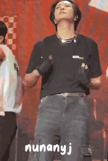 a man in a black shirt is standing on a stage with nunanyj written on the bottom right