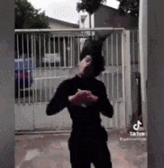 a man in a black shirt is standing in front of a fence and a building .