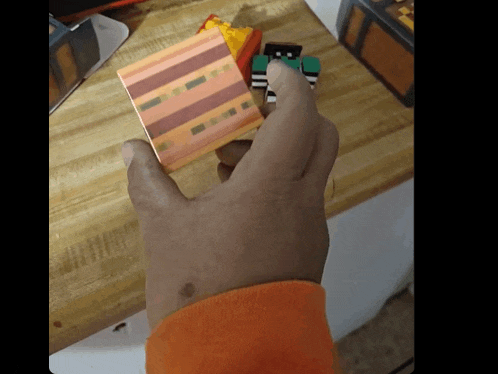 a person 's hand is holding a minecraft figure on a wooden counter top