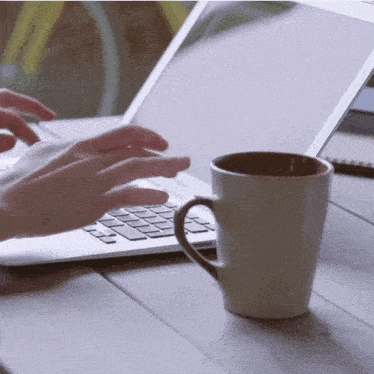 a person is typing on a laptop next to a coffee cup